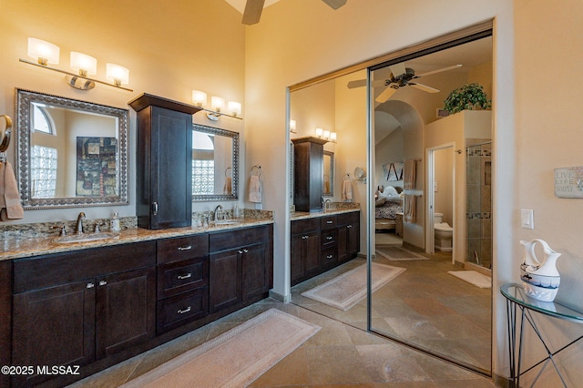 bathroom featuring ceiling fan, vanity, a high ceiling, and toilet