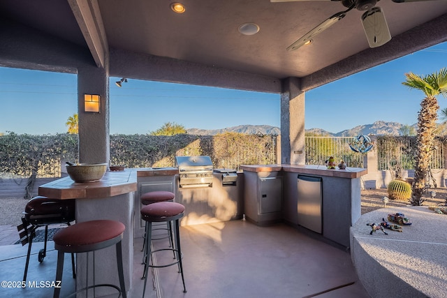 view of patio featuring an outdoor kitchen, area for grilling, ceiling fan, a bar, and a mountain view