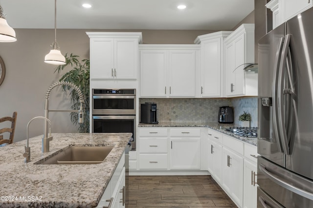 kitchen featuring sink, decorative backsplash, light stone countertops, appliances with stainless steel finishes, and white cabinetry