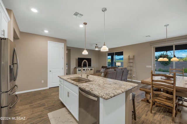 kitchen with light stone countertops, stainless steel appliances, white cabinetry, and an island with sink