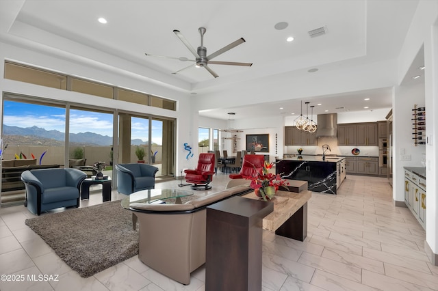 living room with ceiling fan with notable chandelier, a raised ceiling, a mountain view, and sink