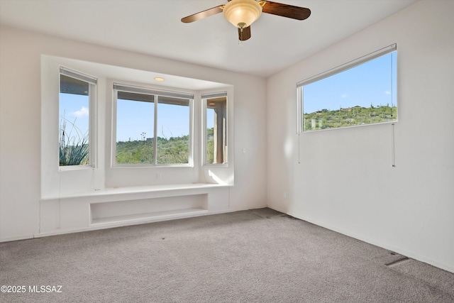 carpeted spare room featuring ceiling fan and a wealth of natural light