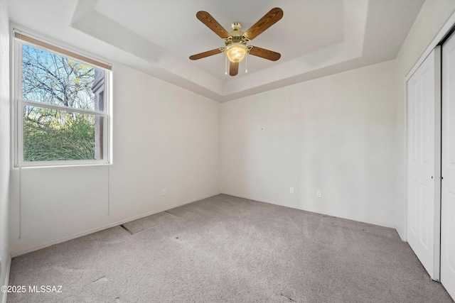 empty room with a raised ceiling, light colored carpet, and ceiling fan