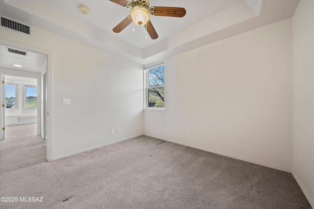 empty room featuring light carpet, ceiling fan, and a tray ceiling