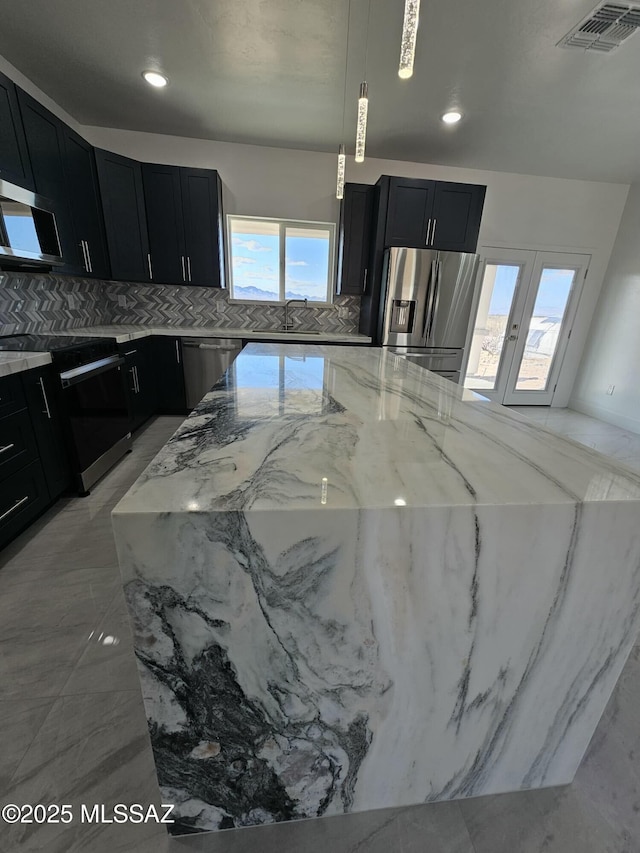 kitchen featuring stainless steel appliances, visible vents, dark cabinetry, and light stone countertops