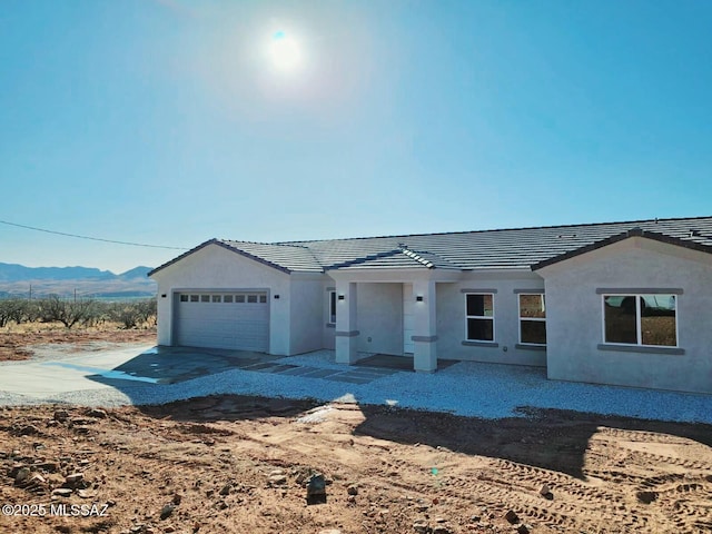 ranch-style home featuring a tiled roof, driveway, a garage, and stucco siding