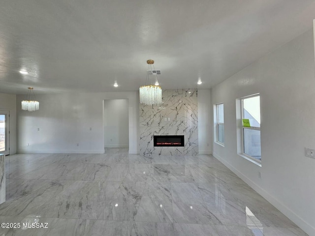 unfurnished living room featuring visible vents, a notable chandelier, baseboards, and a premium fireplace