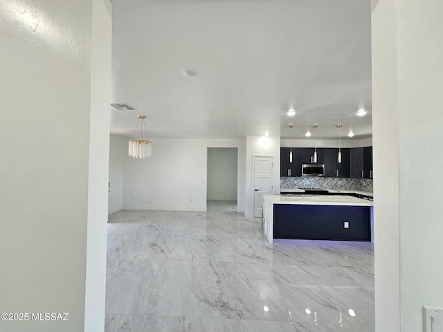 kitchen featuring dark cabinets, visible vents, stainless steel microwave, light countertops, and decorative backsplash