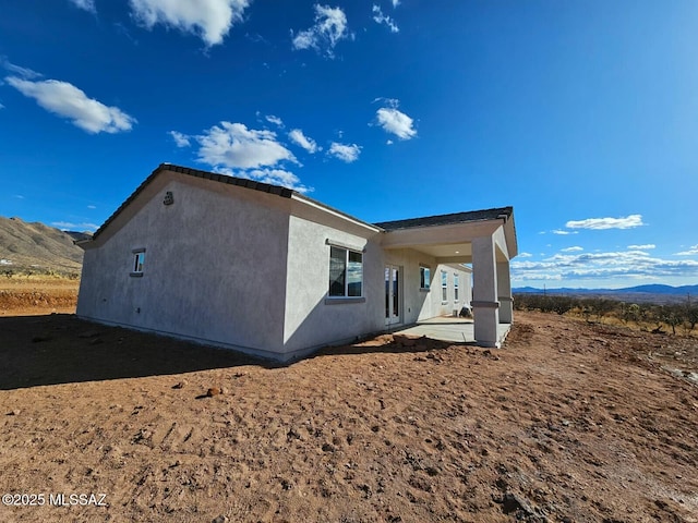 view of side of property with a patio area, a mountain view, and stucco siding