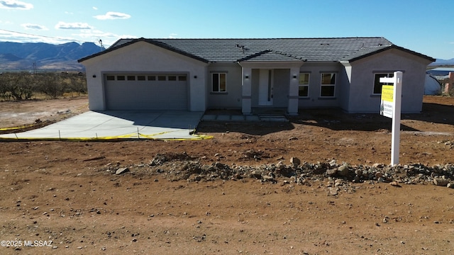 single story home with an attached garage, a mountain view, concrete driveway, and stucco siding