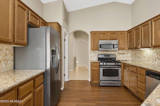 kitchen with backsplash, dark hardwood / wood-style floors, stainless steel appliances, high vaulted ceiling, and light stone counters