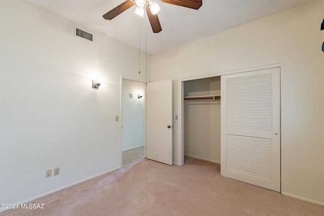 unfurnished bedroom with ceiling fan, a closet, light colored carpet, and a textured ceiling