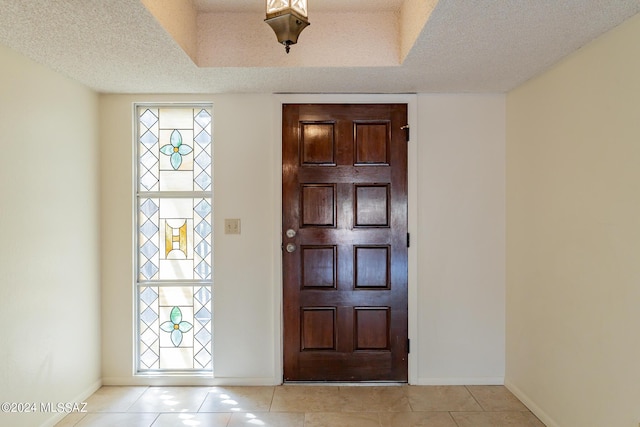 foyer with a raised ceiling, light tile patterned flooring, and a textured ceiling