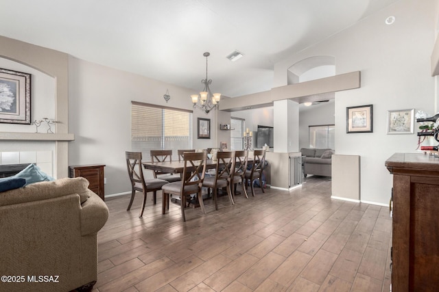 dining area with a tiled fireplace, dark wood-type flooring, lofted ceiling, and a chandelier