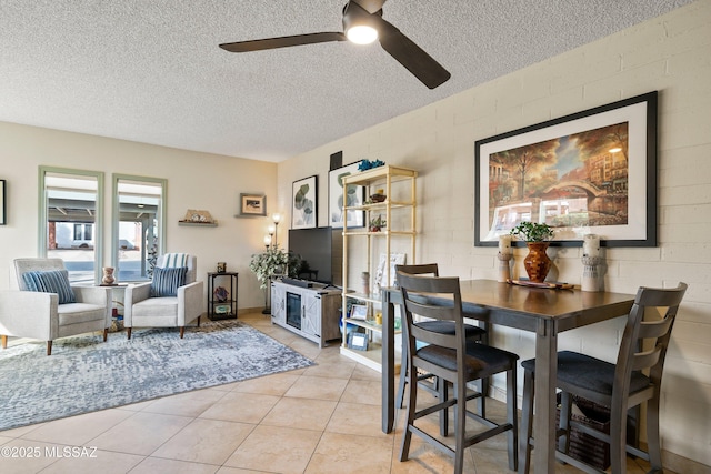 tiled dining space featuring a textured ceiling, ceiling fan, and brick wall