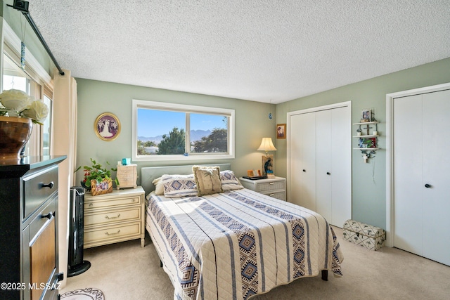 bedroom featuring light carpet, a textured ceiling, and two closets