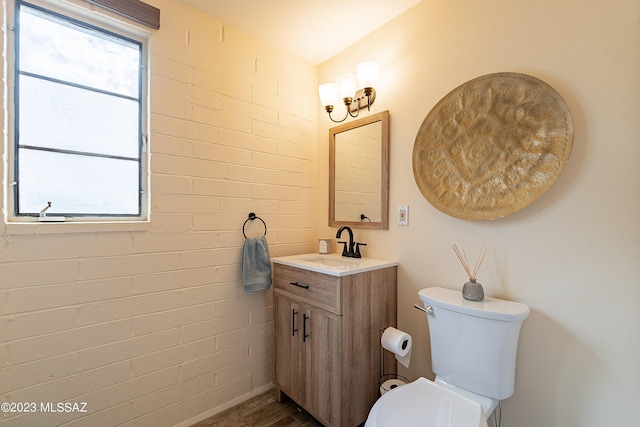 bathroom with vanity, toilet, and brick wall