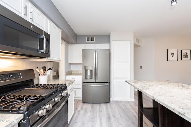 kitchen featuring white cabinets, light hardwood / wood-style flooring, backsplash, light stone countertops, and appliances with stainless steel finishes