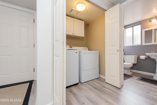 laundry area featuring cabinets, washing machine and clothes dryer, and light hardwood / wood-style floors