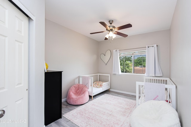 bedroom with ceiling fan, light hardwood / wood-style flooring, and a crib