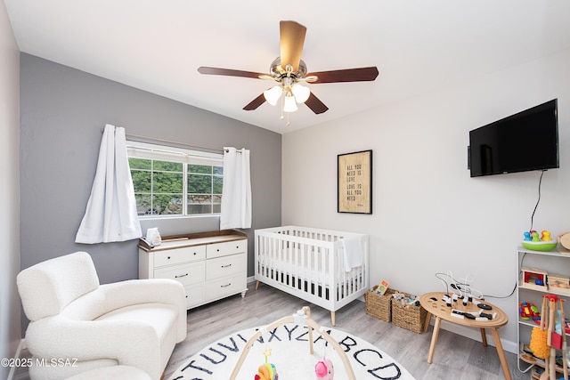 bedroom featuring ceiling fan, a crib, and light hardwood / wood-style flooring