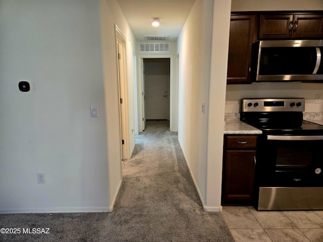 kitchen with dark brown cabinetry, stainless steel appliances, and light carpet