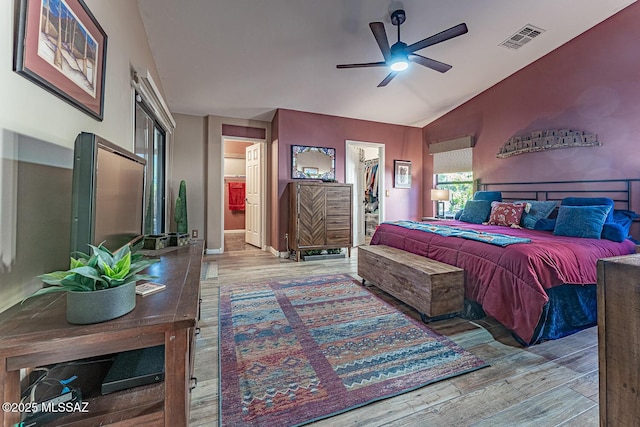 bedroom featuring lofted ceiling, ceiling fan, light wood-type flooring, a closet, and a walk in closet