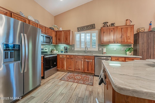 kitchen with stainless steel appliances, sink, backsplash, and light hardwood / wood-style flooring