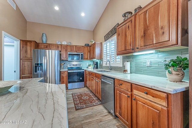 kitchen with light hardwood / wood-style floors, stainless steel appliances, light stone counters, sink, and backsplash