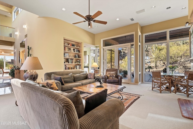 living room featuring ceiling fan, built in features, light colored carpet, and plenty of natural light