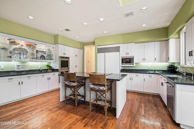 kitchen featuring sink, built in appliances, a kitchen island, dark hardwood / wood-style flooring, and white cabinetry