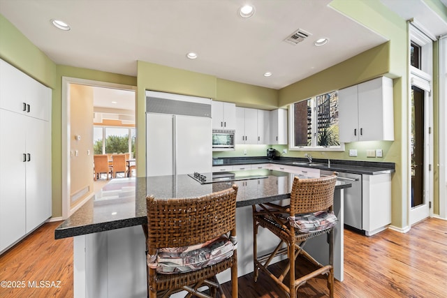 kitchen with stainless steel appliances, white cabinetry, a kitchen island, and light hardwood / wood-style floors