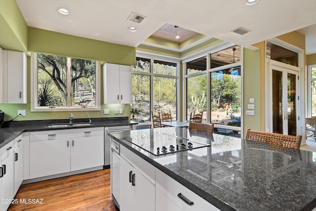 kitchen featuring black electric cooktop, a raised ceiling, sink, dark stone countertops, and white cabinets