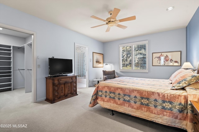 bedroom featuring a spacious closet, a closet, ceiling fan, and light carpet