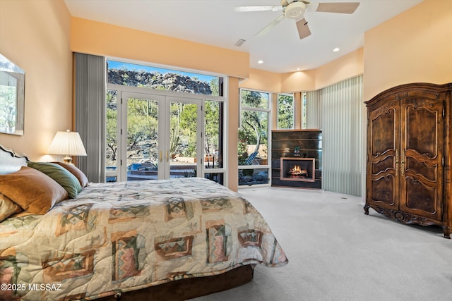 bedroom with carpet, french doors, ceiling fan, access to exterior, and a tiled fireplace