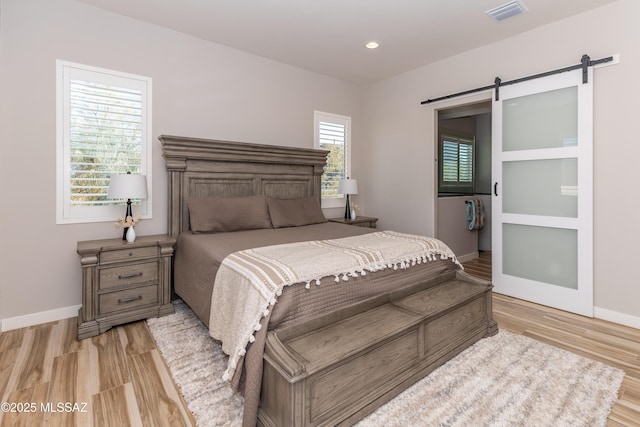 bedroom with a barn door and light wood-type flooring