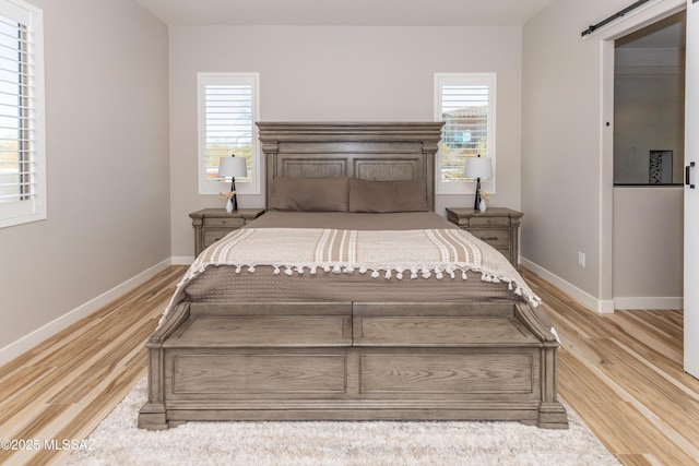 bedroom featuring multiple windows, light hardwood / wood-style flooring, and a barn door