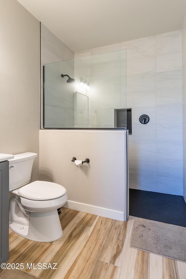 bathroom with hardwood / wood-style floors, vanity, toilet, and a tile shower