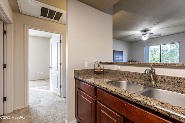 kitchen with ceiling fan, sink, light carpet, and dark stone counters