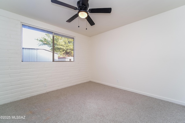 carpeted spare room featuring brick wall and ceiling fan