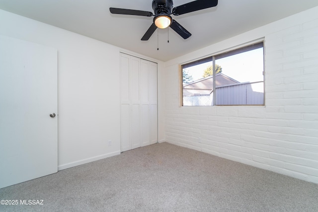 unfurnished bedroom with brick wall, carpet floors, ceiling fan, and a closet