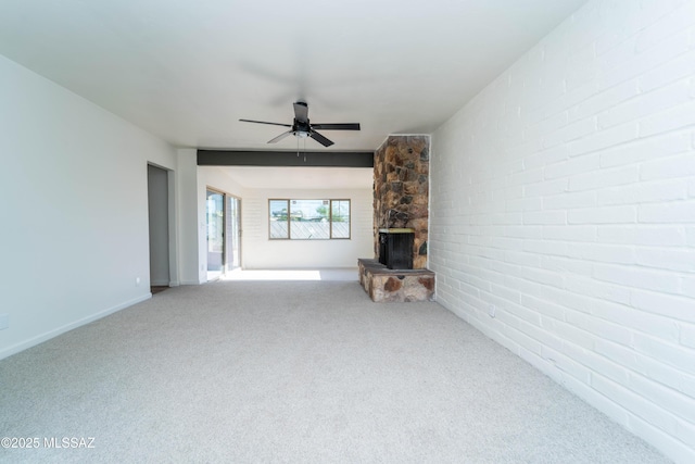 unfurnished living room with ceiling fan, brick wall, a stone fireplace, and carpet floors