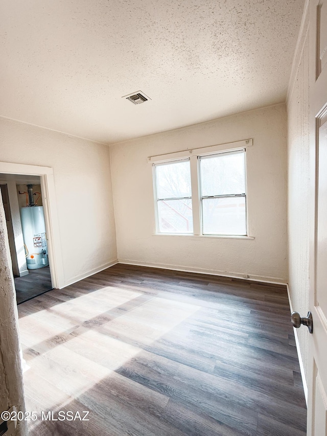 unfurnished room featuring hardwood / wood-style flooring, a textured ceiling, and water heater