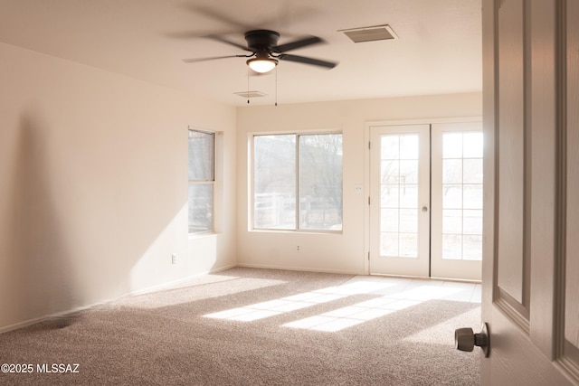 empty room featuring ceiling fan, a healthy amount of sunlight, light colored carpet, and french doors