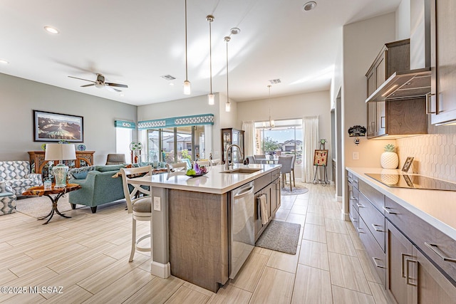 kitchen with ceiling fan with notable chandelier, dishwasher, decorative light fixtures, wall chimney range hood, and an island with sink