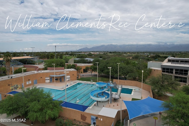 community pool with a water slide, a mountain view, and a patio area