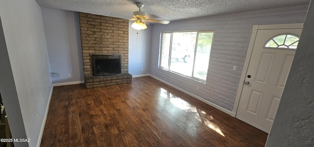 unfurnished living room featuring dark wood-style floors, a textured ceiling, and a brick fireplace