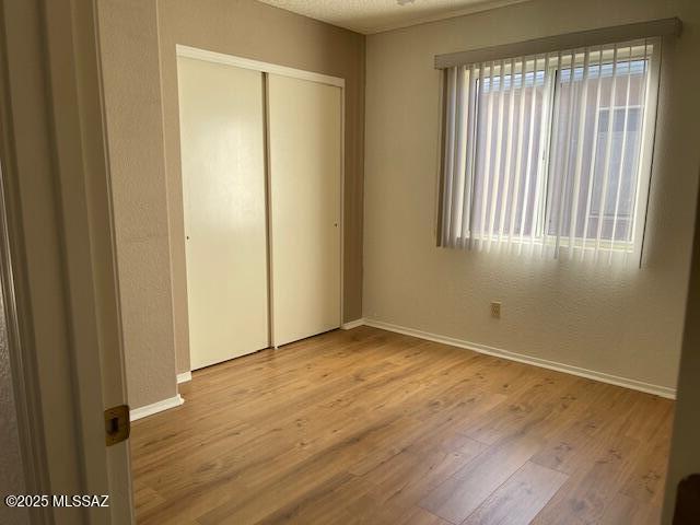 unfurnished bedroom with light wood-type flooring, a textured ceiling, and a closet