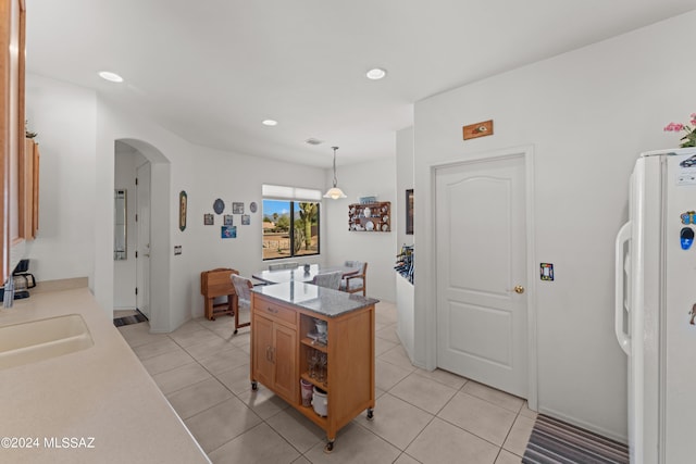 kitchen featuring arched walkways, pendant lighting, recessed lighting, freestanding refrigerator, and a sink