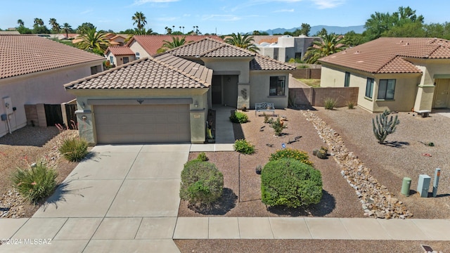 mediterranean / spanish house featuring stucco siding, an attached garage, fence, driveway, and a tiled roof